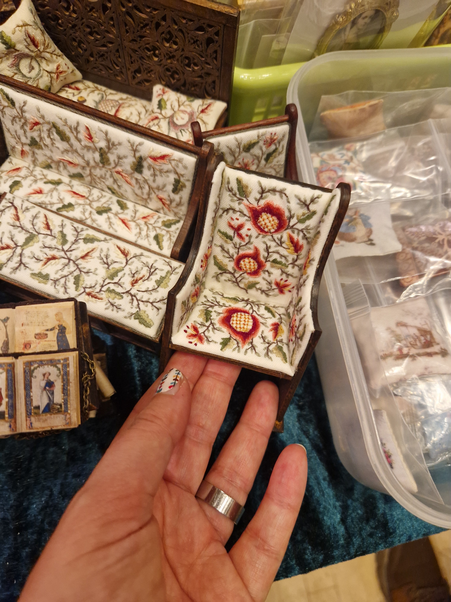 Mano sostiene una silla en miniatura con tapizado bordado floral rojo y verde.