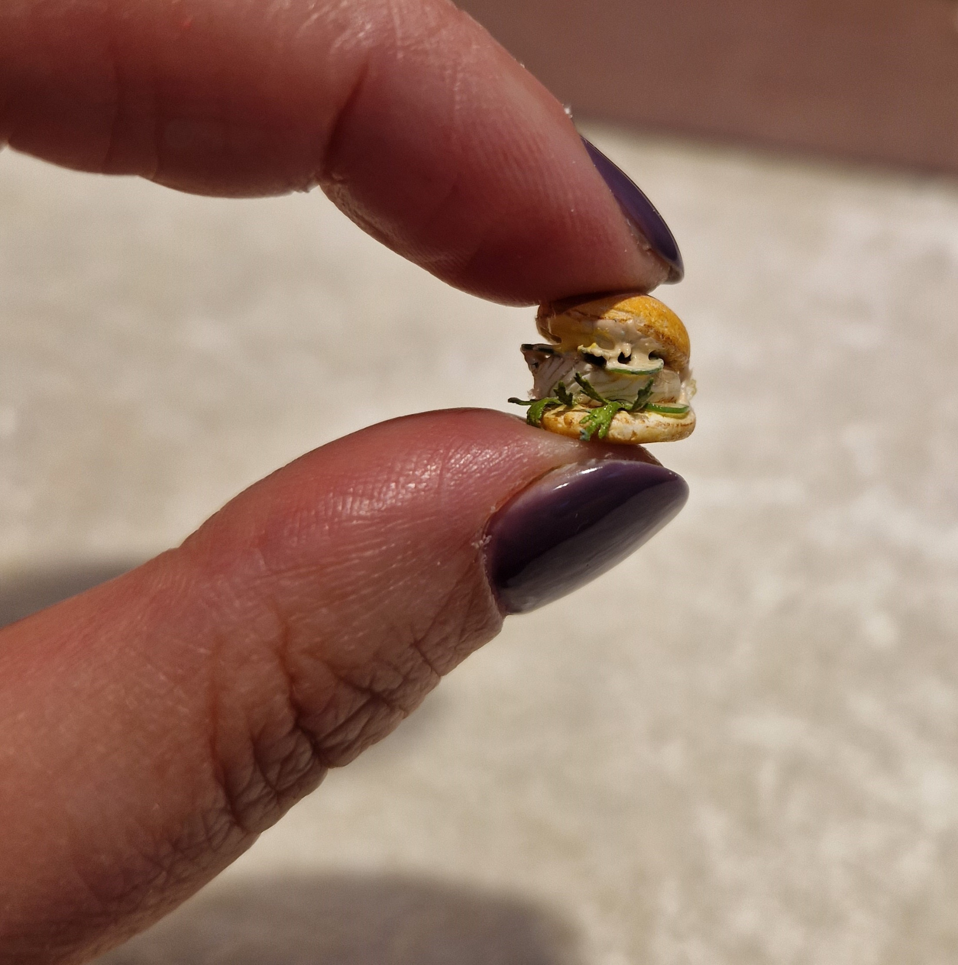 Mano sostiene una hamburguesa en miniatura.