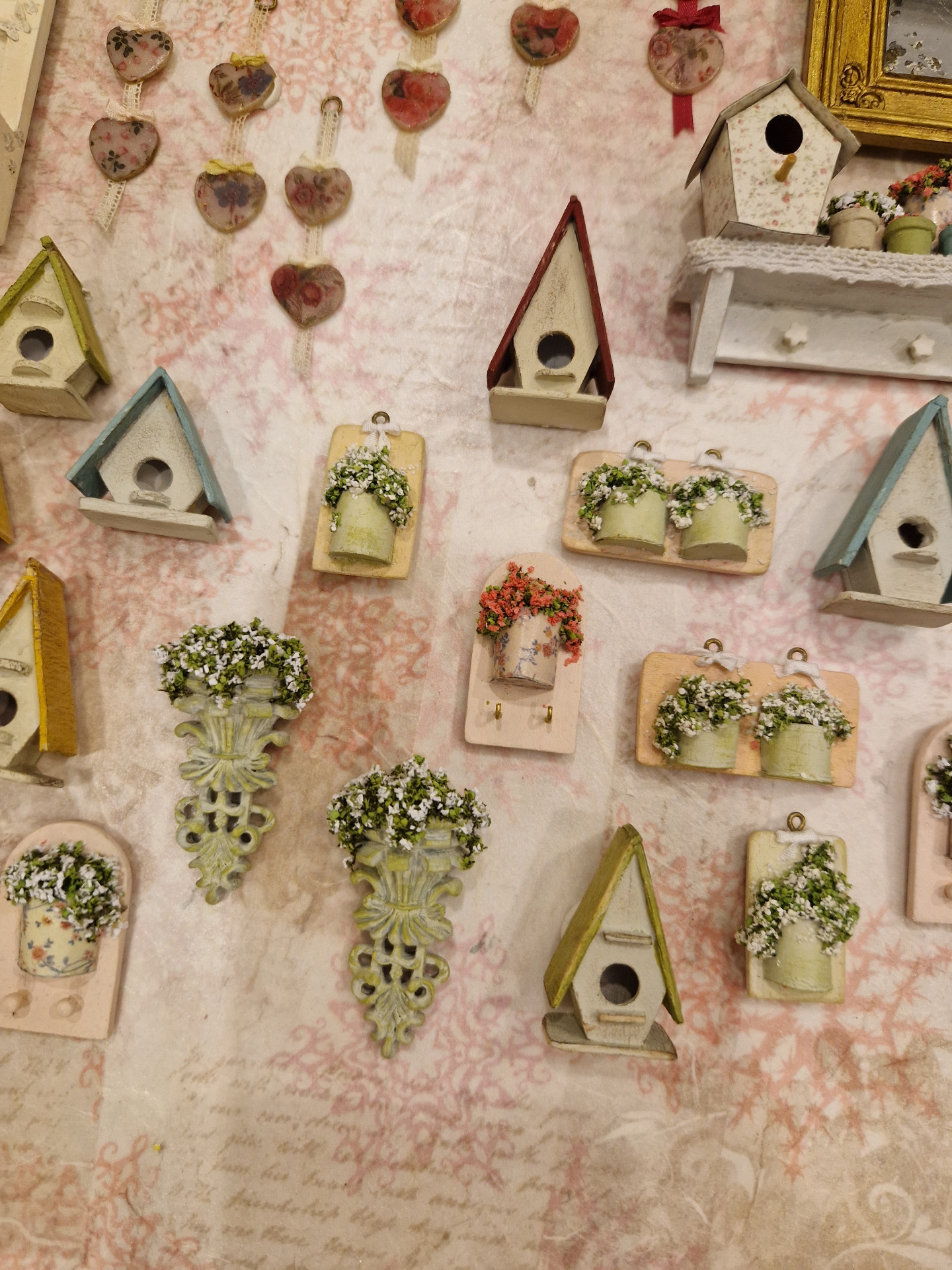 Casitas de pájaros y otras decoraciones en miniatura, colgadas sobre fondo rosa estampado.